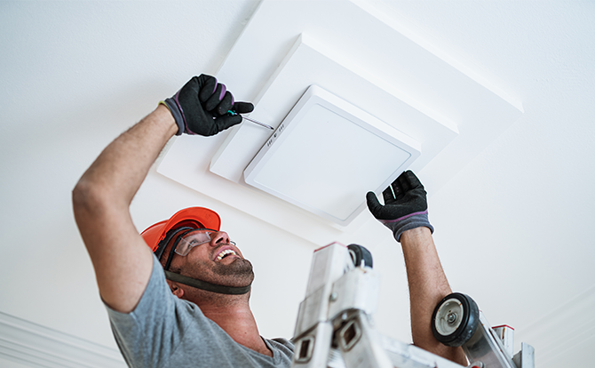 homme souriant qui installe un luminaire au plafond